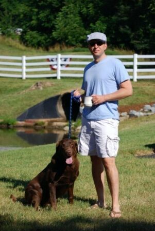 A man and his brown lab in grass.