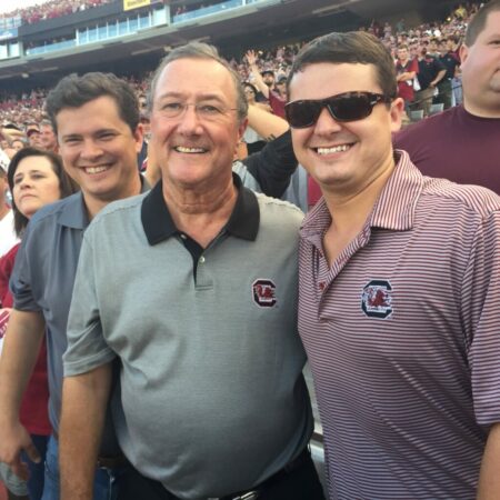 A father and two son's smiling at a USC football game.