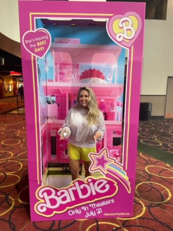 A lady in a barbie box posing like barbie smiling.