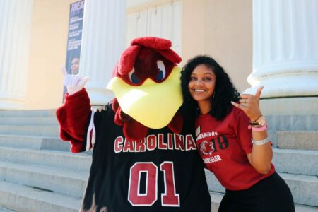 A woman and cocky the mascot posing outside of UofSC theater.