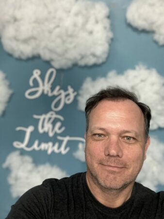 Man posing in front of "sky's the limit" sign.