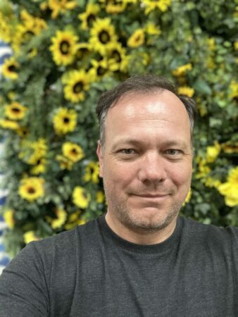 A man smiling in front of a wall of sunflowers.
