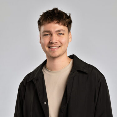 Headshot of young man in tan shirt and dark jacket