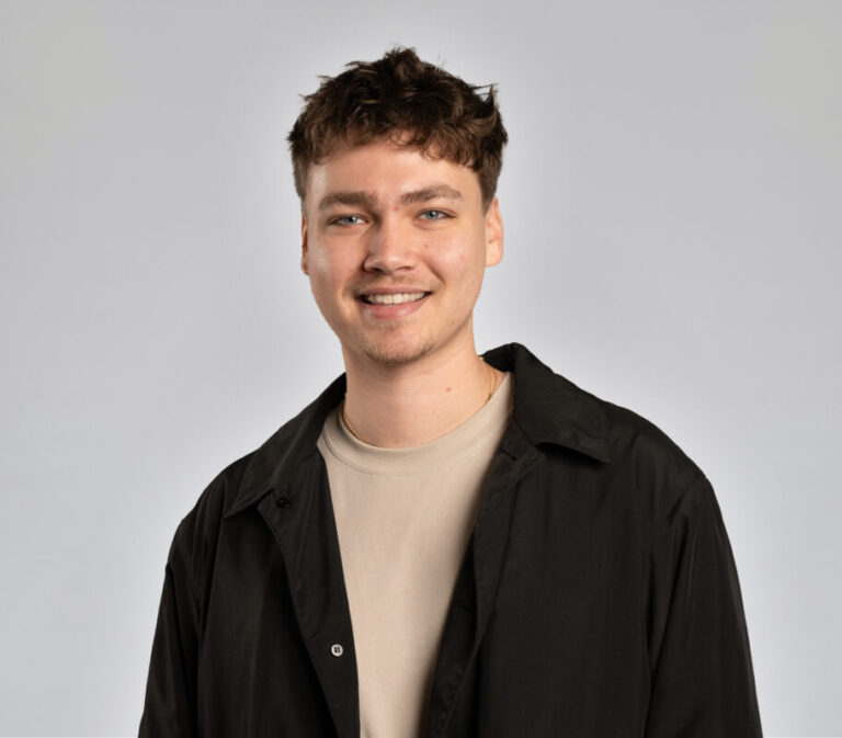 Headshot of young man in tan shirt and dark jacket