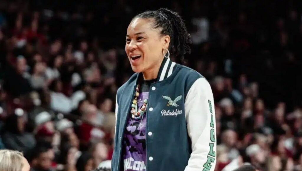 Coach Dawn Staley wearing a Philadelphia Eagles jacket with the out of focus image of a crowd at a basketball arena behind